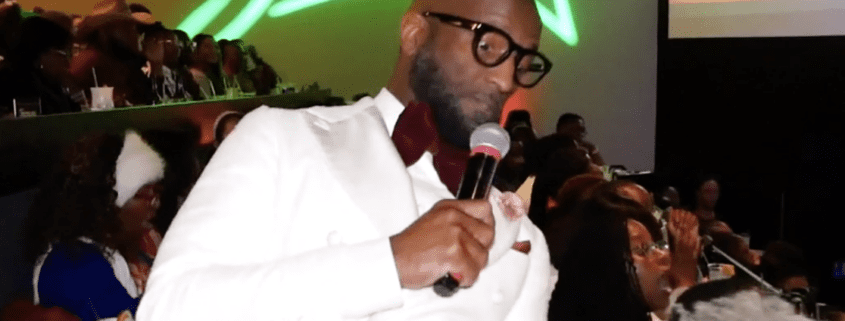 Man in white suit speaking into microphone.